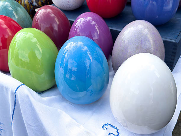 Colorful display of glazed ceramic eggs on white fabric tablecloth.