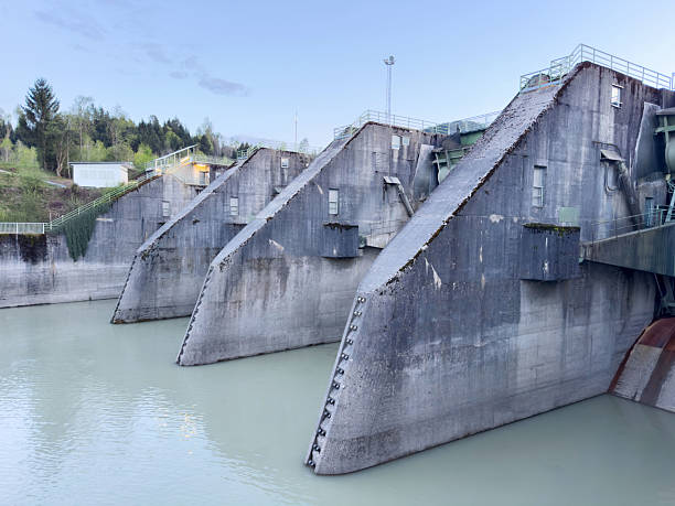 istock Large concrete dam structure on calm river with green forest in background 2211420087