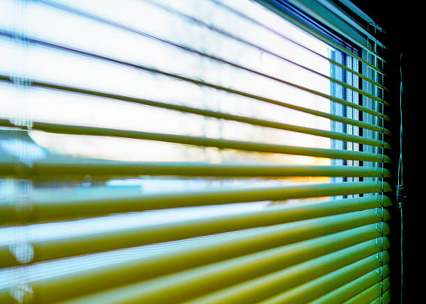 Look through blinds on sunrise. Green Blinds to secretly look through window. Bedroom window, opening curtains. Looking through window blinds, morning sun light coming inside of room. Windowshade.