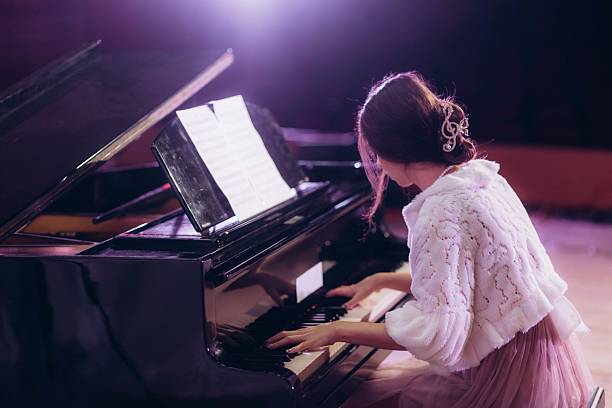 istock Woman Playing Piano in Elegant Attire Under Warm Lighting in a Performance Hall 2211422607