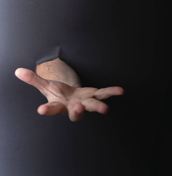 istock photo Mysterious hand reaching through a solid surface in a dramatic and surreal gesture suggesting help, support, or connection in an abstract and intriguing artistic setting. 2211429542