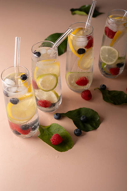 istock refreshing summer beverage with citrus and berries in clear glasses on soft pink surface, featuring ice cubes, leaves, lemons, limes, raspberries, blueberries, and straws, zesty, invigorating 2211430946