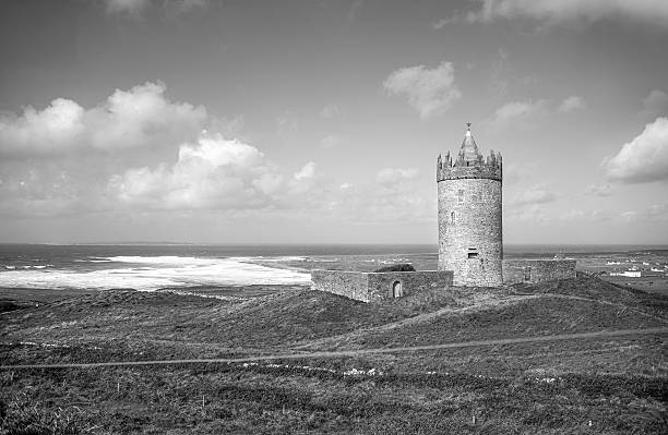 Dublin, Ireland - September 1, 2023 - Doonagore Castle, the 16th-century, cylindrical, sandstone tower house near Doolin Point, looks out over the wind-blown waves of the Atlantic Ocean toward Inisheer Island. Lush green fields surround the structure, adding to the serene and picturesque landscape on a sunny, summer day in County Clare, Ireland.