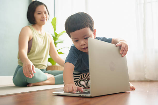 istock Asian Young boy curiously using a laptop while his mother watches, both sitting on a yoga mat 2211435984