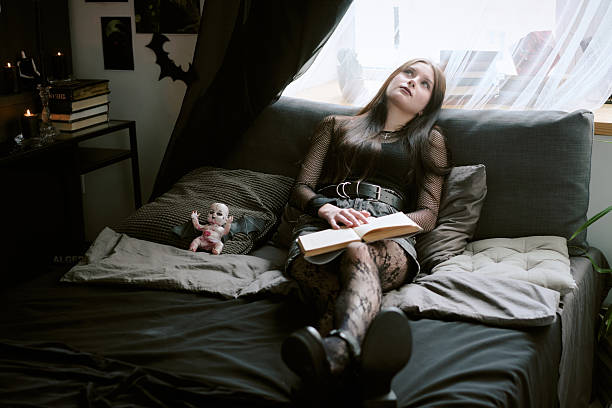 Goth teen girl in black clothes holding favorite boo in hands while imaging scene from mysterious novel