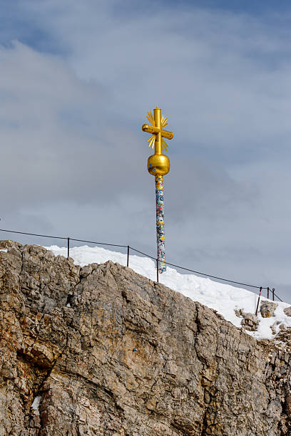 Metal Christian cross on top of mountain above clouds in serene sky