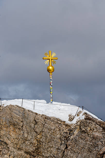 Golden cross of Zugspitze in blue and sinny sky, some birds are flying around.