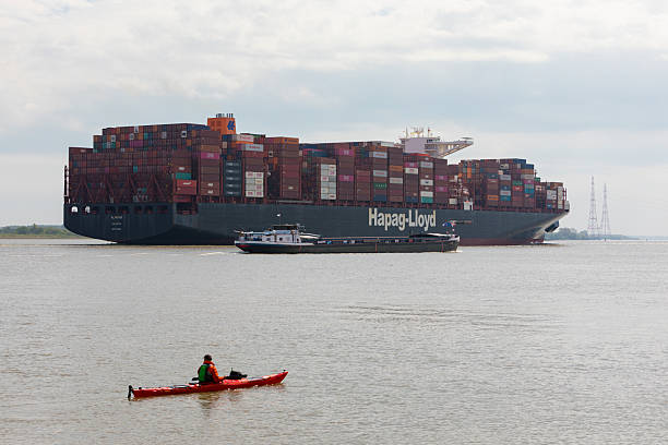 Stade, Germany – May 11, 2022: Ultra-large container ship AL NEFUD,  operated by Hapag-Lloyd,  on Elbe river heading to Hamburg, passing by a bulk carrier and a canoeist