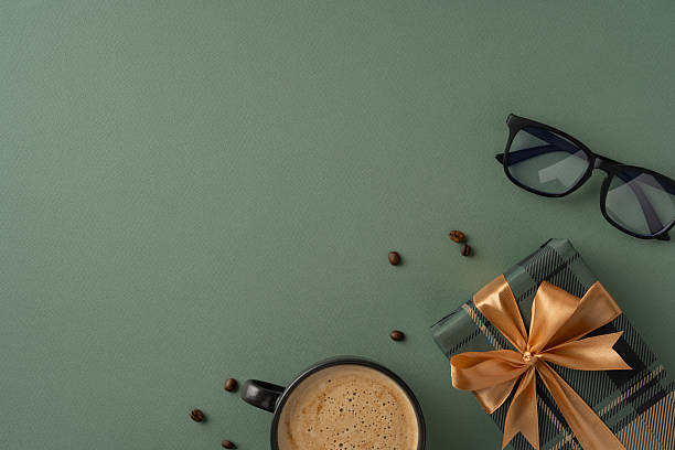 istock Scene featuring a present wrapped in gold ribbon, alongside coffee and glasses on green backdrop 2211449189