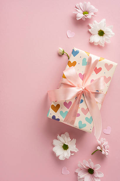 istock Gift box wrapped in heart-patterned vertical paper with a ribbon, surrounded by white flowers 2211449198