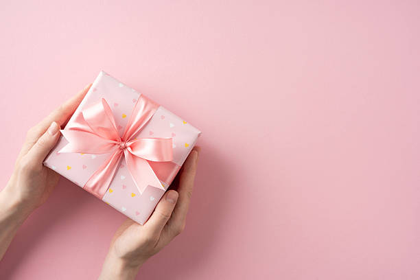 istock A delicate pink gift box adorned with a satin ribbon, held gently in hands, conveying an aura of love and care, perfect for celebrating special occasions, birthdays, holidays, or moments of affection 2211449207