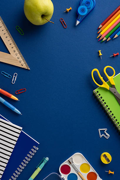 istock Stationery vertical items including notebooks, pencils, scissors, and an apple arranged on a blue surface 2211449237