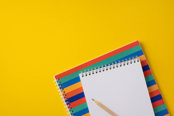 istock Notebook with a pencil placed on a vibrant, colorful striped surface against yellow. 2211449312