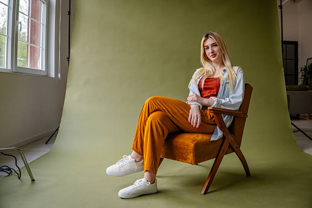 Pensive sad teen girl sitting sideways on a comfortable armchair and looking at camera, copy space