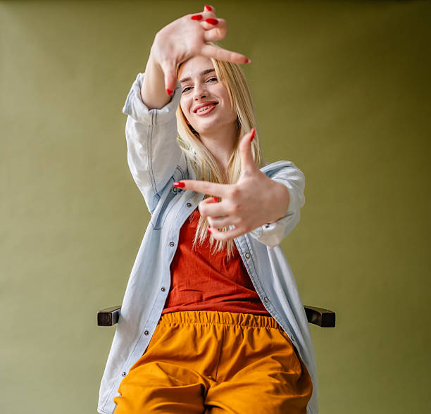 Bright and stylish young blonde woman smiles while showcasing a playful pose in a well-lit studio setting. She exudes confidence and happiness, making the atmosphere lively and inviting.