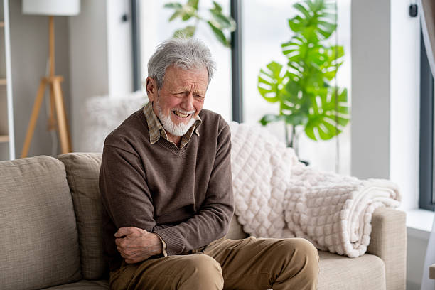istock Elderly Individual with Pained Expression on Living Room Couch 2211451401