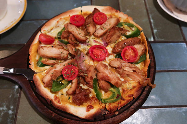 close up of a grilled chicken pieces, green pepper, cherry tomato and cheese pizza on a serving board