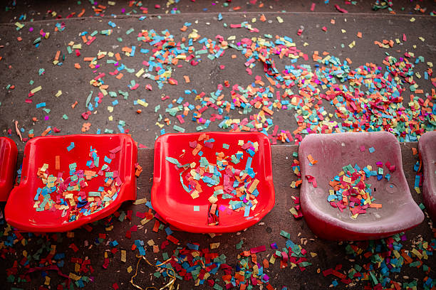 Stadium stands are left dirty and abandoned after a soccer match, with broken chairs and scattered colorful confetti highlighting the aftermath of the event.