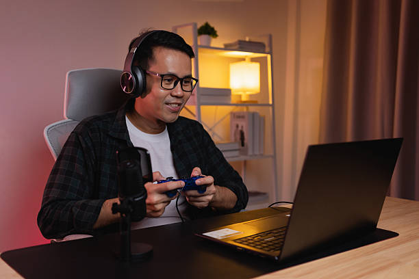 istock Young man enjoying video game play with headset and controller in modern gaming setup with laptop and ambient lighting in cozy indoor space 2211455431