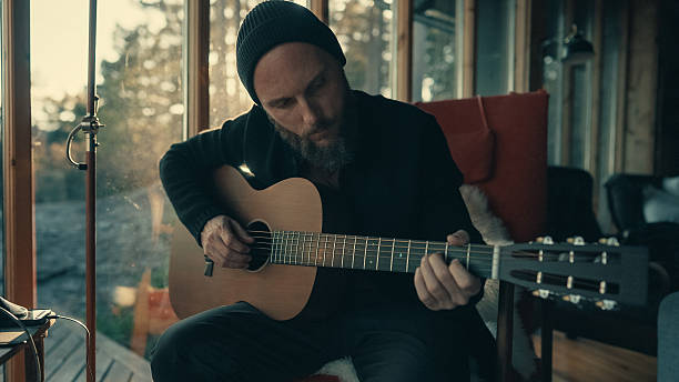 istock Man playing acoustic guitar inside cozy cabin 2211467357