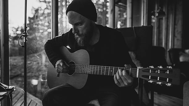 Man playing acoustic guitar inside cozy cabin, with soft sunlight streaming through the window.