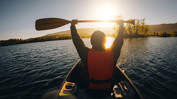 istock Man paddling a canoe on a calm lake at sunset 2211469426
