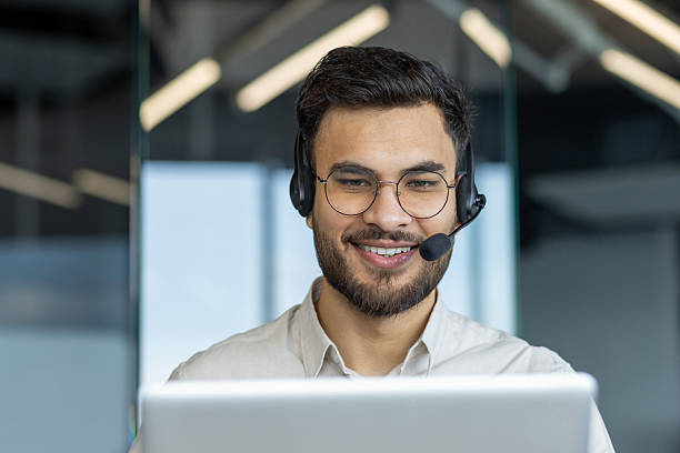istock Man with headset close-up smiling, talking and consulting clients remotely. Support service worker at workplace inside office. Consultant at work 2211469766