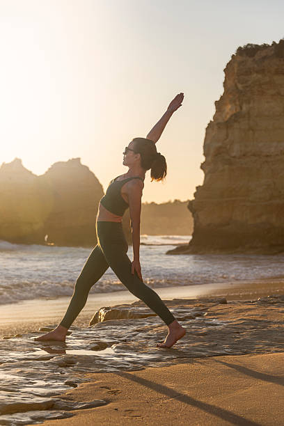 sporty woman practicing yoga by the sea doing a reverse warrior pose