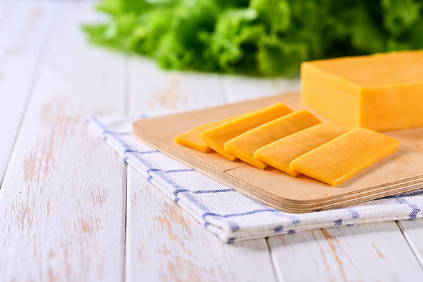 istock pieces of yellow cheddar cheese on a white wooden table, copy space for text. 2211471133