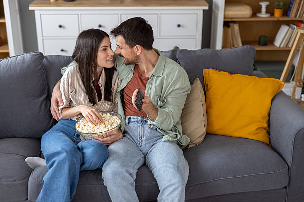 istock Couple Laughing While Eating Popcorn on the Couch Together 2211472904