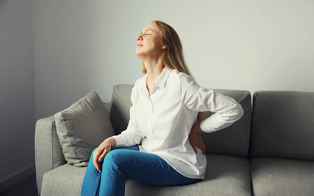 istock Woman suffering from back pain while sitting on couch at home 2211473247