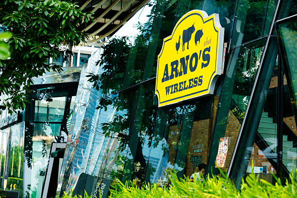 French steak restaurant in basement of  modern designed  Sindhorn Tower with Starbucks coffee shop in background  in Wittayu Road in Bangkok downtown. Coffee shop iand steak restaurant called Arno's Wirless are located in basement of Sindhorn Tower with some other restaurants. Inside are a few people. View from northern side and  sidewalk
