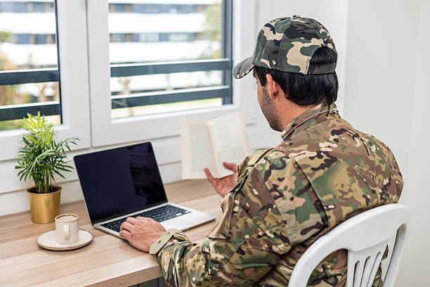 istock Soldier teleworking from home reading a book and using laptop 2211475046