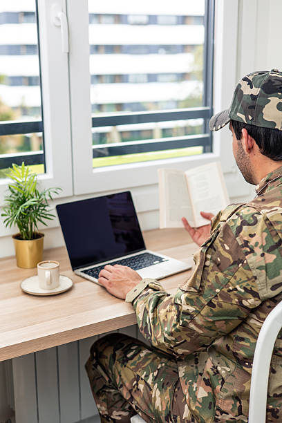 istock Soldier teleworking from home office using laptop and reading book 2211475050