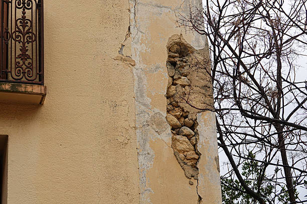 A building wall reveals damage with exposed stones and peeling plaster