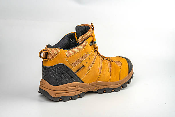 Image of a high-top hiking boot on light gray background, designed for rugged terrain with sturdy construction and ankle support Color scheme includes brown, black, and yellow or orange accents Lik