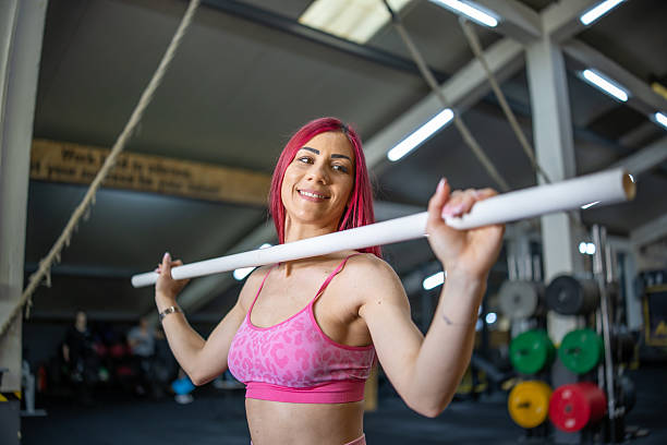 istock Smiling woman in sportswear warming up for training and doing exercise with gymnastic stick in the gym. 2211491415