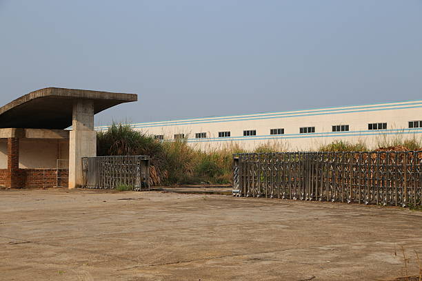 istock A large abandoned warehouse with an open gate is surrounded by wild grasses. 2211506615