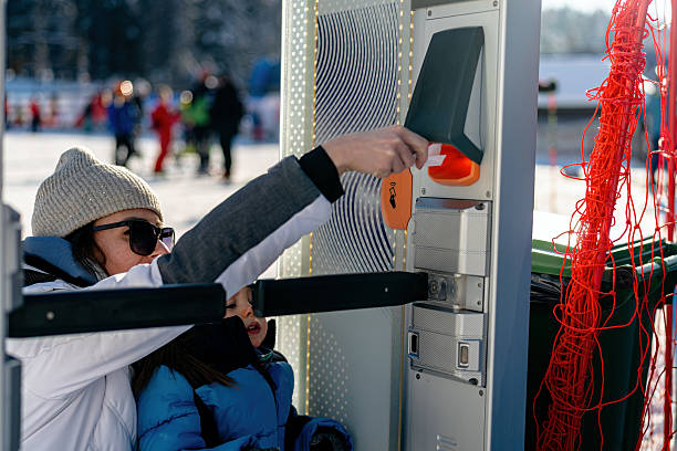 A parent helps their child activate an access point using an entry card on a sunny winter day. The environment features a playful atmosphere with other individuals in the background enjoying the outdoors.