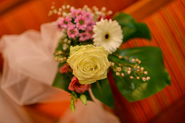 A warm-toned close-up of a wedding bouquet featuring white, pink, and green blossoms. Shot indoors with warm directional light, the image captures the richness and harmony of the floral arrangement.