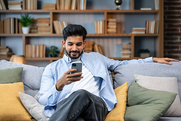 istock Young indian man holding smartphone tech device using cell phone apps at home. Bearded ethnic guy texting messages looking at smartphone checking social media, ordering online or browsing. 2211510236