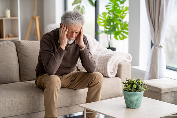 istock Elderly man holding his head in distress on a sofa 2211517337
