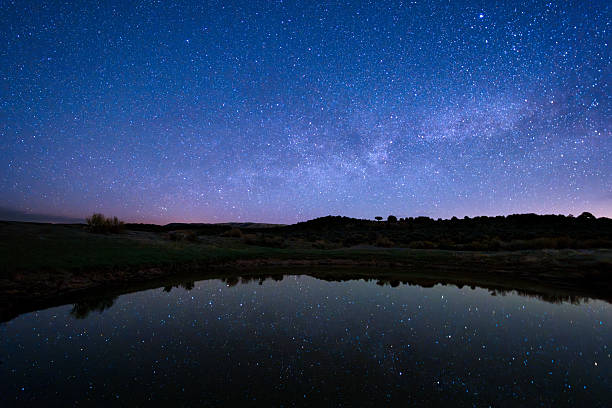 Lyrid Meteor Shower Astrophotography Night Landscape - Scenic dark sky mountain landscape with small lake reflecting stars and galaxy. High desert mountain area with sky of crisp bright stars.