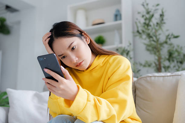 istock Bad news on device screen. Upset asian woman frustrated by problem with work or relationships, sitting on couch, feeling despair and anxiety, loneliness, having psychological trouble 2211523521