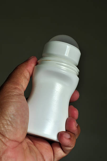 istock Close-up of a person's hand holding a white plastic roll-on deodorant container against a dark green background 2211528871