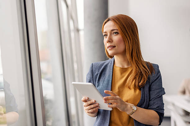 istock Female business expert with tablet in hands looking through the window while standing at corporate office. 2211530888
