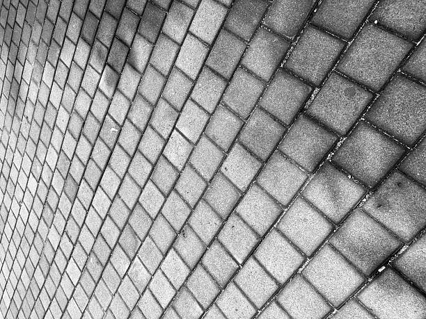 Black and white pattern of interlocking concrete paving blocks forming a geometric street surface.