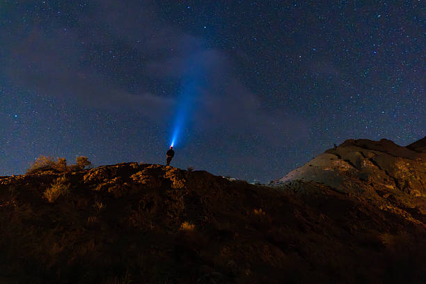 Man Exploring Dark Skies with Headlight and Light Beam Projecting in to Space - Scenic dark sky area with man standing atop mountain canyon ridge peering up into a sky full of stars with blue light beam in sky.