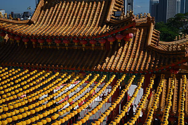A vibrant view of a traditional Chinese temple with intricate architecture and tiled roofs, adorned with red lanterns, set against the backdrop of a modern city skyline with towering skyscrapers. The temple's ornate details, including carved stone railings, contrast beautifully with the urban landscape, capturing the blend of cultural heritage and contemporary life.