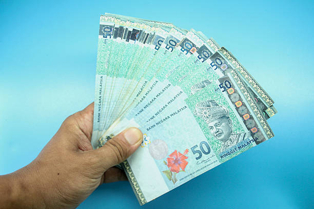 istock Malaysia Currency (MYR): Stacking of 50 Ringgit Malaysia bank note on hand which isolated with blue background 2211541419